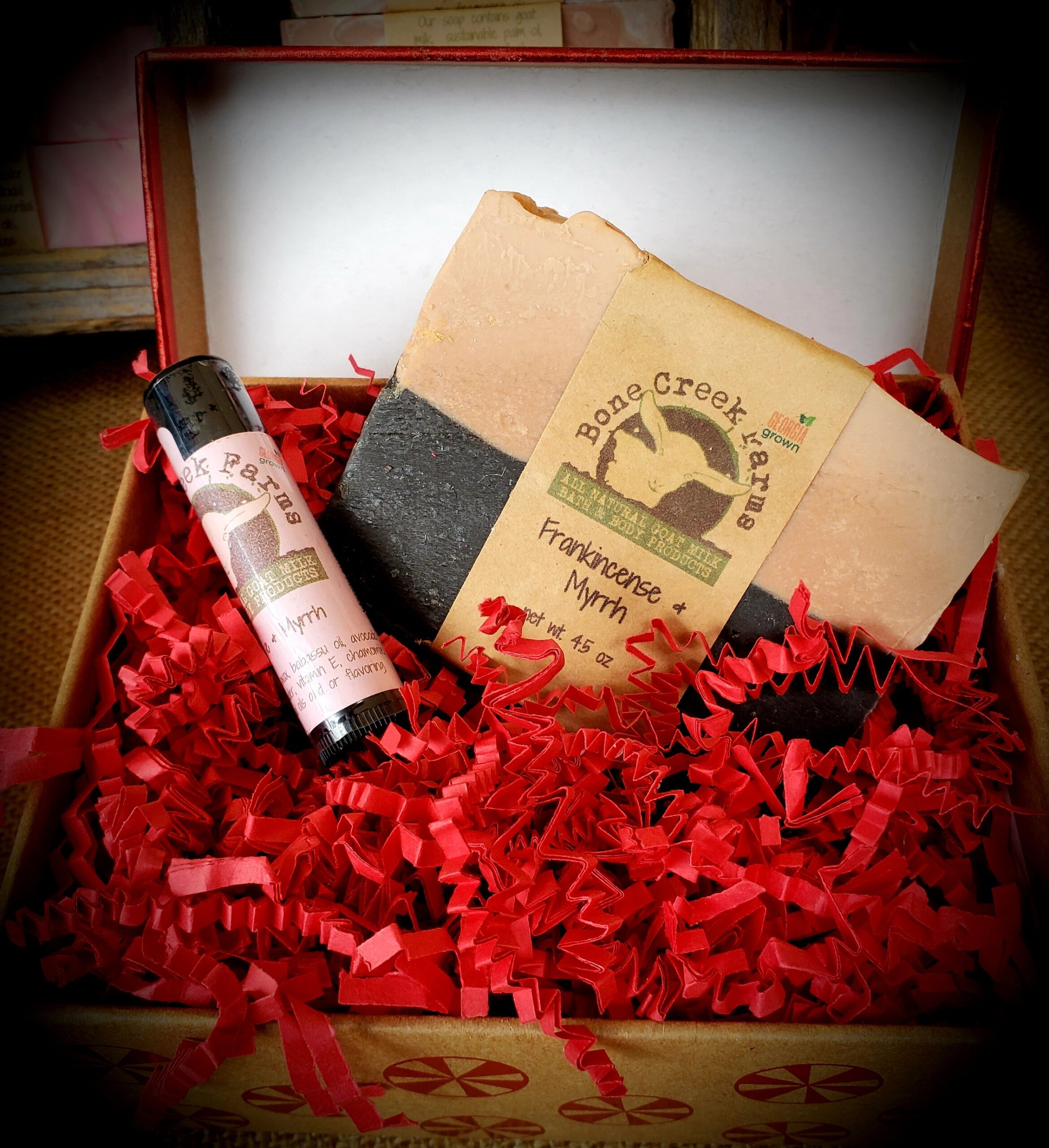 Tisha+Carr+-+20181215_142101 Gift box featuring Bone Creek Farms natural frankincense and myrrh soap alongside a matching essential oil roller. The box is filled with red crinkle paper, highlighting the handmade, organic skincare products.
