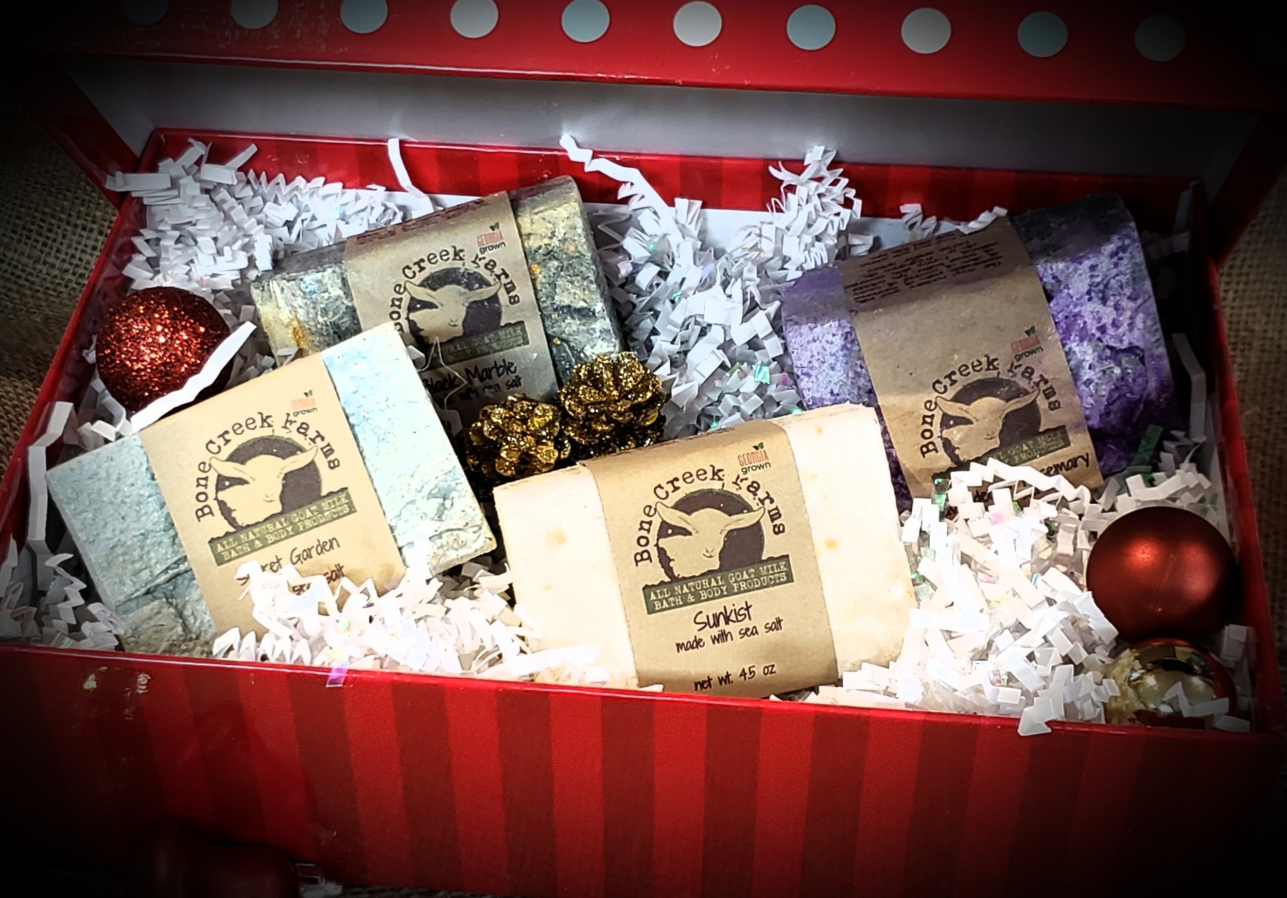 Tisha+Carr+-+20181219_125629 Gift box containing assorted all-natural goat milk soaps from Bone Creek Farm, including varieties like Sweet Garden and Sunkist, presented with decorative elements and shredded paper filler.