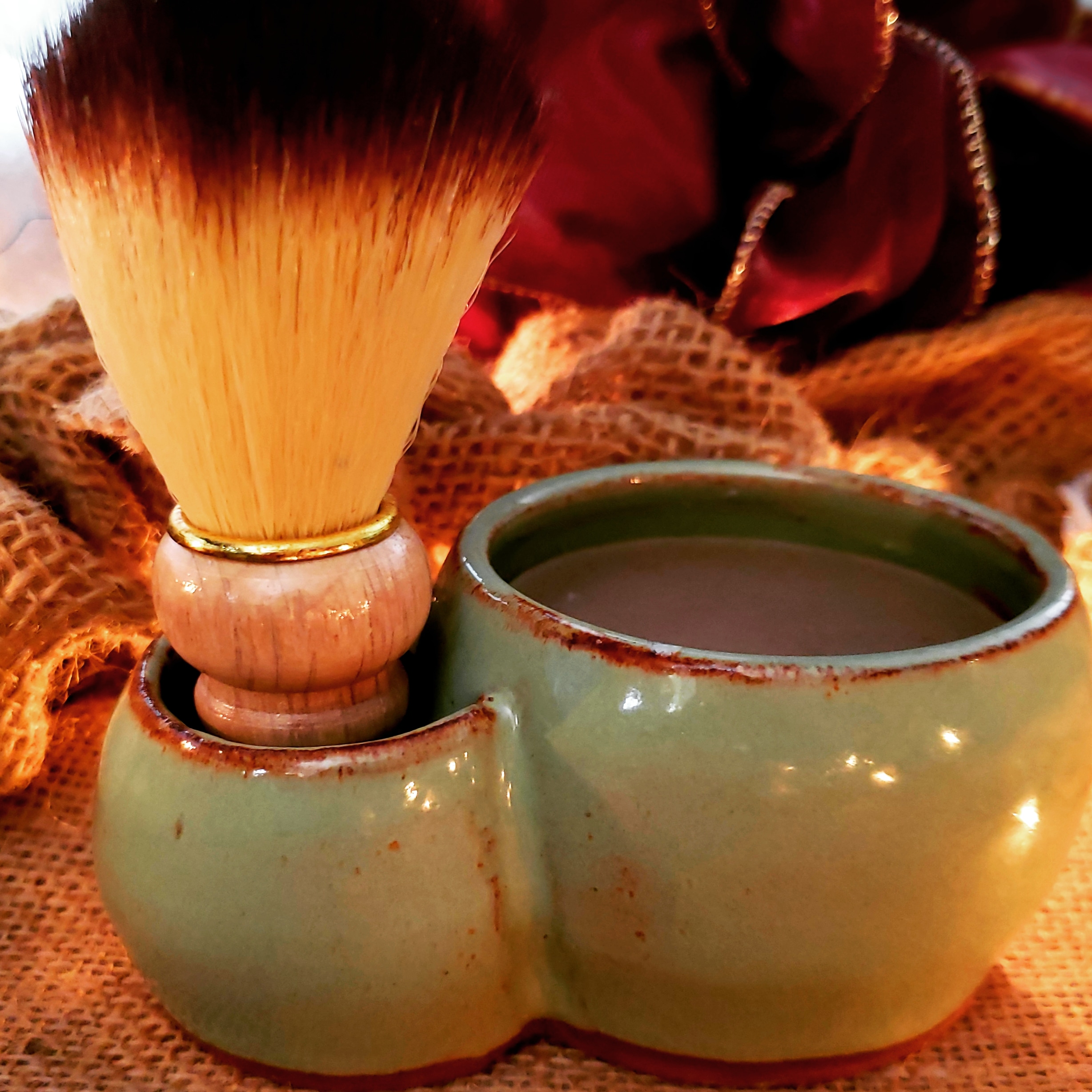 Tisha+Carr+-+IMG_20181205_120453_919 Ceramic shaving bowl with a wooden-handled brush, featuring soft bristles, placed on burlap fabric. Ideal for traditional wet shaving enthusiasts.